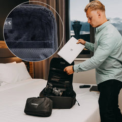 Scapade AirPack opened flat on a hotel bed like a suitcase, with a laptop slipped into the padded sleeve